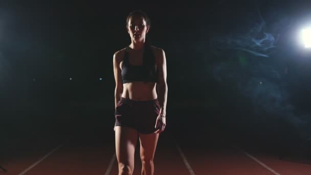 暗い背景にスタジアムのトラックでスニーカーでジョギング シューズのスプリントを実行する暗い背景の gotovtes にプロの女性アスリート。平均プラン — ストック動画