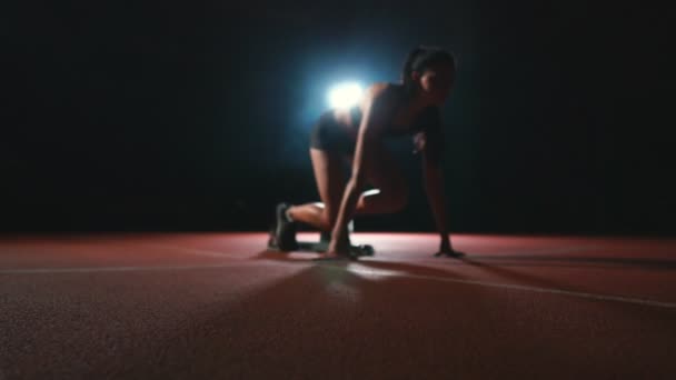 Mujer atleta profesional sobre un fondo oscuro para correr el sprint de los zapatos de correr en zapatillas de deporte en la pista del estadio sobre un fondo oscuro — Vídeo de stock