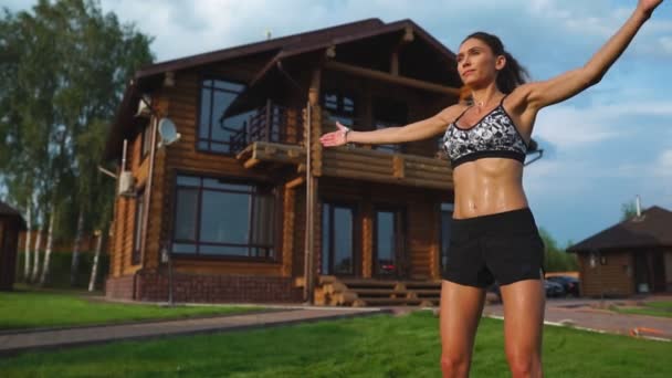 Mujer hermosa delgada en ropa deportiva en el fondo de la casa en el césped realiza saltos para el entrenamiento cardiovascular y la quema de grasa — Vídeos de Stock