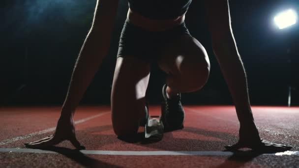 Professionele vrouw atleet op een donkere achtergrond gotovtes uit te voeren van de sprint van Jogging schoenen in sneakers op het spoor van het stadion op een donkere achtergrond. Close-up — Stockvideo