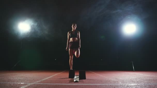 职业女子运动员在一个黑暗的背景 gotovtes 跑的短跑鞋运动鞋在体育场的轨道上的黑暗背景。平均计划 — 图库视频影像