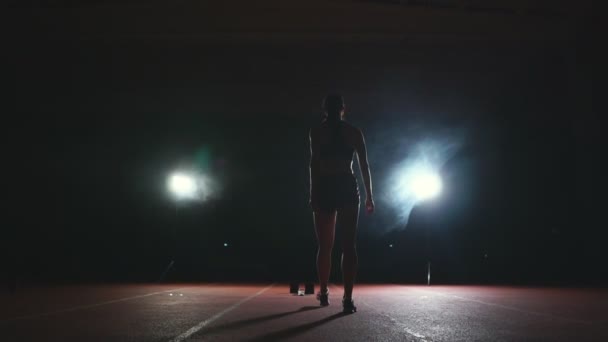 Mujer atleta profesional sobre un fondo oscuro para correr el sprint de los zapatos de correr en zapatillas de deporte en la pista del estadio sobre un fondo oscuro — Vídeo de stock