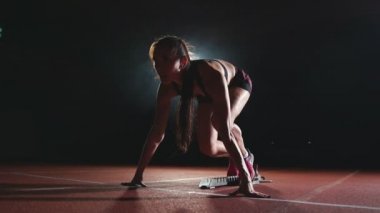 Koşu ayakkabıları sprint spor ayakkabı içinde stadyumun parça koyu arka plan üzerinde çalıştırmak için profesyonel kadın atlet karanlık bir arka plan üzerinde