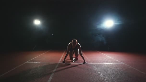 Atletka na tmavém pozadí se chystá spustit běžecké sprint z podložky na běžeckém pásu na tmavém pozadí — Stock video