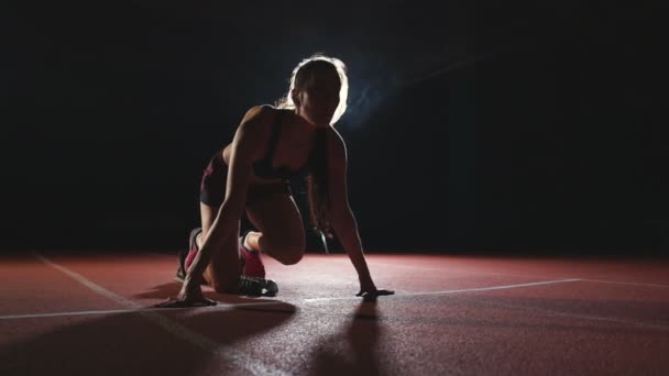 Professionell kvinna idrottsman på en mörk bakgrund gotovtes att köra sprinten Jogging skor i sneakers på spår på stadion på en mörk bakgrund. Genomsnittliga plan — Stockvideo