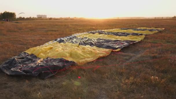 Paracaídas tirados en el suelo en los rayos del sol al atardecer en el aeródromo — Vídeo de stock