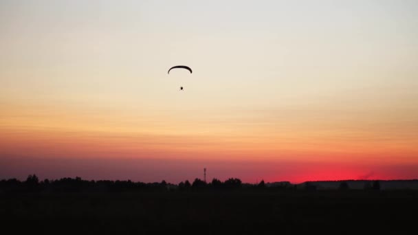 O piloto em um parapente voa da câmera gradualmente afastando-se na distância contra o pôr do sol belo céu. Imagem de fundo bonito fundo. conceito de liberdade — Vídeo de Stock