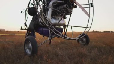 Günbatımı güneş ışınlarının havaalanında motorlu yamaçparaşütü duruyor. Uçağın arka planda çıkartıyor. Kamera yörünge hareket eder.