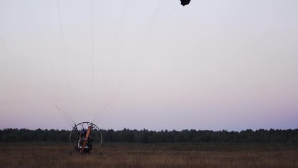 De motor paraglider verlaagt de parachute na de landing en stopt helemaal in het veld na zonsondergang — Stockvideo