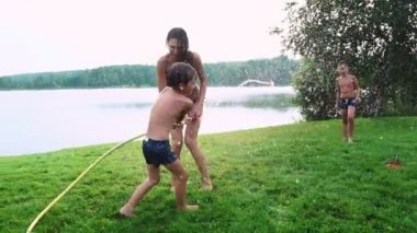 Anne baba ve iki oğlu çim yaz aylarında çim için bir hortum su döktü. Alan kır evi yakın bir göl günbatımı