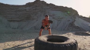 Kas atlet güçlü adam adam ağır çekimde kumlu dağlar büyük bir tekerlek üzerinde çekiç vurur. güç ve dayanıklılık eğitim güreşçiler için