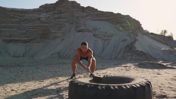 Muscle athlète homme fort homme frappe un marteau sur une énorme roue dans les montagnes sablonneuses au ralenti. entraînement de force et d'endurance pour les lutteurs — Video