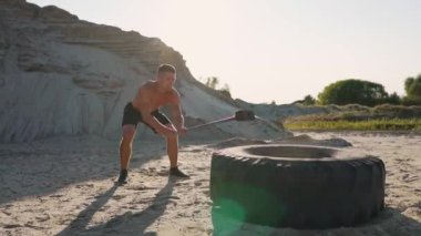 Kas atlet güçlü adam adam ağır çekimde kumlu dağlar büyük bir tekerlek üzerinde çekiç vurur. güç ve dayanıklılık eğitim güreşçiler için