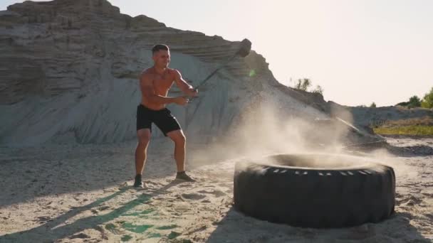 Atleta muscular homem forte bate um martelo em uma roda enorme nas montanhas arenosas em câmera lenta. treinamento de força e resistência para lutadores — Vídeo de Stock