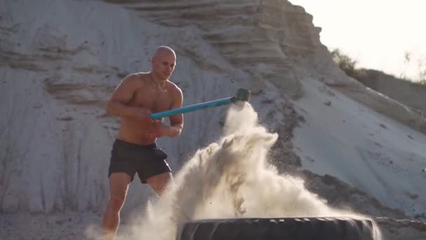 Homme chauve homme fort frappe un marteau sur une énorme roue dans les montagnes de sable au ralenti. entraînement de force et d'endurance pour les lutteurs . — Video
