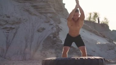 Kas atlet güçlü adam adam bir çekiç kumlu dağlar yavaş hareket büyük bir tekerlek üzerinde günbatımında vurur. Tekerlekleri tozdan yükselir.