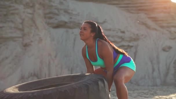 Chica en una cantera de arena empujando una rueda en entrenamiento crossfit entrenamiento al atardecer en el sol — Vídeos de Stock