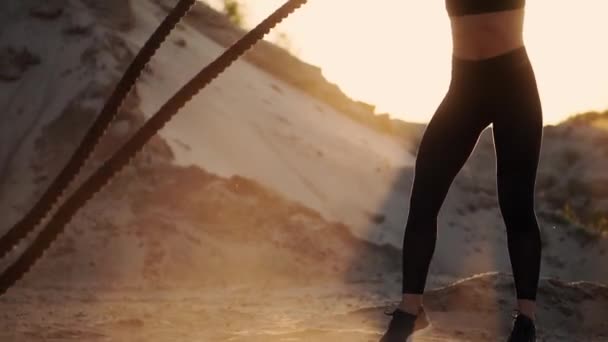 Close-up de uma menina com uma corda realiza treinamento ao ar livre no chão arenoso perto da praia. Corda nas mãos das mulheres ao pôr do sol — Vídeo de Stock