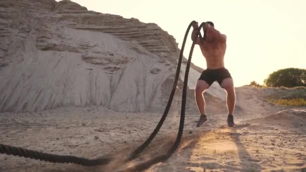 Hombre atleta empuje-UPS en la playa y golpea el suelo con una cuerda, entrenamiento circular en el sol en una playa de arena . — Vídeos de Stock