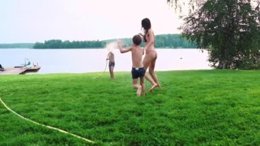Iki çocuk anne ve baba hortum su ile drenching ve gülüyor ve ağır çekimde gülümseyen evlerinin arka bahçesinde oynuyorlar. Mutlu bir aile