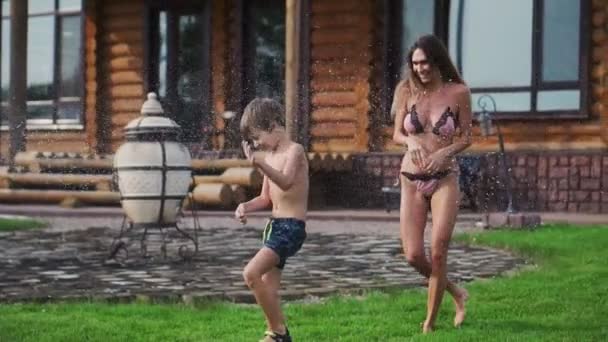 Madre e padre che giocano con i bambini sul prato della casa versando acqua da un tubo — Video Stock