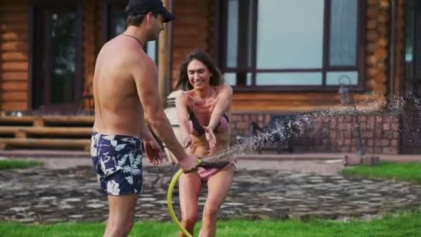 Mor och far leker med barn på gräsmattan av huset hälla vatten från en slang — Stockvideo