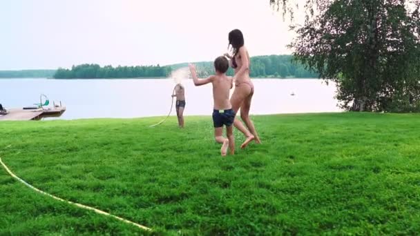 De två pojkarna leker med mamma och pappa på bakgården av deras hus dränkte med slang vatten och skrattar och ler i slow motion. Lycklig familj — Stockvideo