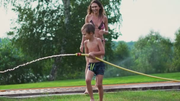 Mama i syn, grając na trawnik wlewając wodę śmiechu i zabawy na placu zabaw z trawnikiem na tle jego domu w pobliżu jeziora — Wideo stockowe