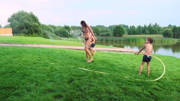 I due ragazzi stanno giocando con mamma e papà nel cortile della loro casa inzuppati di acqua del tubo e ridendo e sorridendo al rallentatore. Famiglia felice — Video Stock