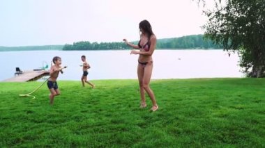 Anne ve oğlu gülen ve having fun evinin arka planda bir çim bahçesi olarak su çim dökme oynarken göle yakın: