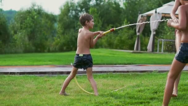 De twee jongens spelen met vader en moeder in de achtertuin van hun huis met slang water drenken en lachen en glimlachen in slow motion. Gelukkige familie — Stockvideo