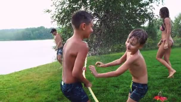 Mãe com pai e duas crianças brincando no gramado derramando água rindo e se divertindo no Playground com gramado no fundo de sua casa perto do lago em câmera lenta — Vídeo de Stock