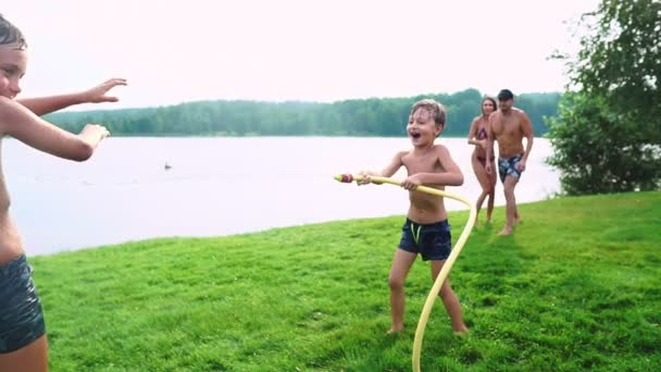 An einem sonnigen Sommertag auf der Liegewiese haben Familie mit zwei Kindern Spaß beim Wasserspielen und Lachen. fröhliche Atmosphäre einer glücklichen Familie — Stockvideo