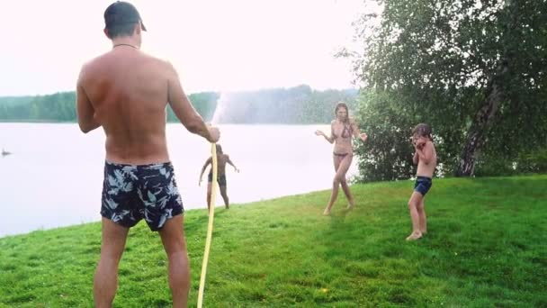 Family in the backyard of a country house in the summer relax playing with water and hosing — Stock Video