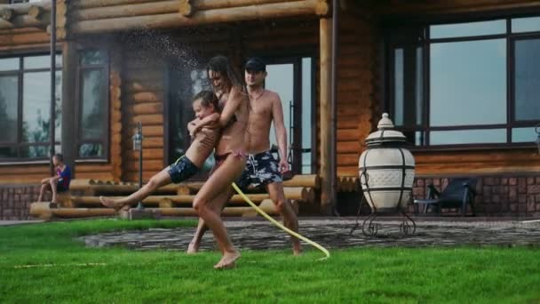Familia en el patio trasero de una casa de campo en el verano relajarse jugando con agua y manguera — Vídeo de stock