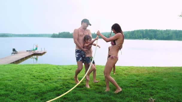 Mom dad and two sons in the summer on the grass poured water from a hose for the lawn. Area country house near a lake at sunset — Stock Video