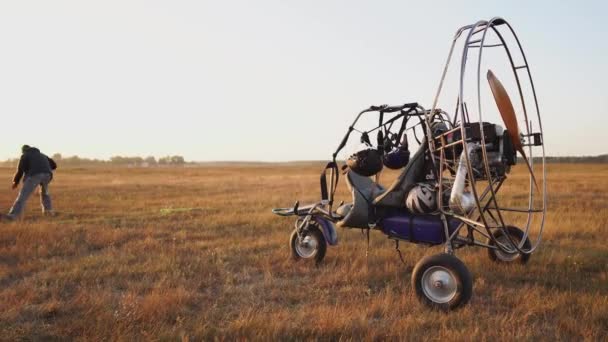 Il parapendio motore sta in campo al tramonto con un'elica di legno, e il pilota stende il paracadute e allinea le imbragature. — Video Stock