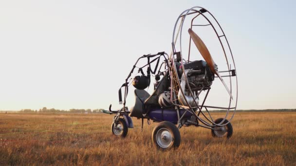 Der Motorgleitschirm steht bei Sonnenuntergang mit einem hölzernen Propeller auf dem Feld, und der Pilot legt den Fallschirm aus und richtet die Schlingen aus — Stockvideo