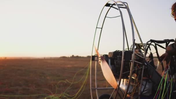 Человек пилот парапланерист фиксирует парашют к телу параплана на закате в поле — стоковое видео