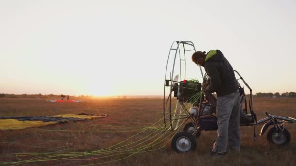 De piloot van een man van een motor paraglider hecht de parachute aan het lichaam van de paraglider vlucht voorbereiden en controleren van apparatuur — Stockvideo