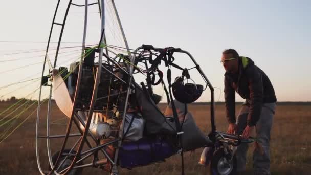 A man pilot of a motor paraglider attaches the parachute to the body of the paraglider preparing for flight and checking equipment — Stock Video