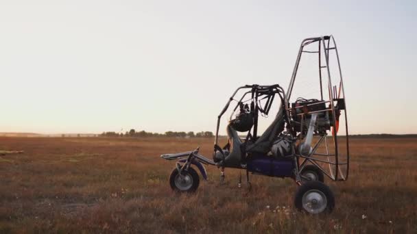 Motor paraglider staat op de luchthaven in de zonsondergang zonnestralen. Op de achtergrond opstijgt het vliegtuig. De camera beweegt langs de baan — Stockvideo