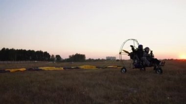 Bir kız ve bir adam havaalanında hızlandırılması ve paraşütle gökyüzüne havalandığını motorlu yamaçparaşütü çıkartıyor.