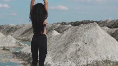Siyah spor giyim trenler mavi su ile beyaz tebeşir kum ocağı karşı sportif esmer kız. Siyah saçlı kız onun elleri ve mesafe içine görünüyor cliff zam geliyor