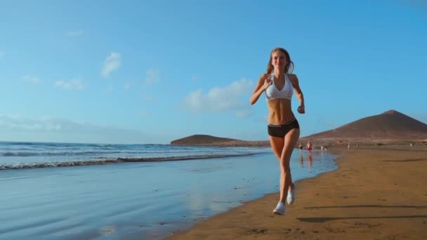 Hermosa mujer deportiva corriendo a lo largo de la hermosa playa de arena, estilo de vida saludable, disfrutando de vacaciones de verano activas cerca del mar. en cámara lenta — Vídeos de Stock