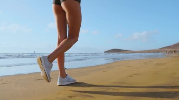 Primo piano della donna sportiva gamba in scarpe da ginnastica bianche che corrono lungo la bella spiaggia di sabbia, stile di vita sano al rallentatore — Video Stock