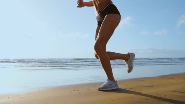 Крупный план ноги спортивной женщины в белых кроссовках, бегущей вдоль прекрасного песчаного пляжа, здорового образа жизни. in slow motion — стоковое видео
