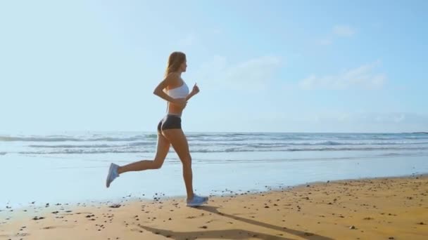 Mladá žena s štíhlá postava se zabývá gymnastika na moři při západu slunce. Ona dělá běh podél mořského pobřeží. sekvence fotoaparát stabilizátor střely. Zpomalený pohyb Steadicam. — Stock video