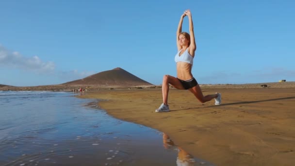 Retiro y entrenamiento de yoga: la mujer en yoga posa en la playa al amanecer. Chica de yoga femenina entrenando en un paisaje oceánico sereno. STEADICAM DE MOVIMIENTO Lento — Vídeo de stock