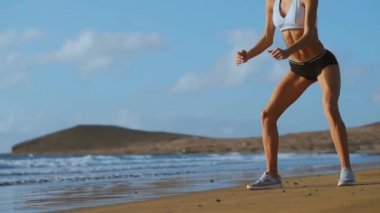 Çekirdek ve glutes plajda bodur egzersizleri yapıyor vücut ağırlığı egzersiz ile çalışan genç kadın fitness. sportif kız çömelme bacaklar aktif ve formda bir yaşamın bir parçası olarak. stedicam ateş